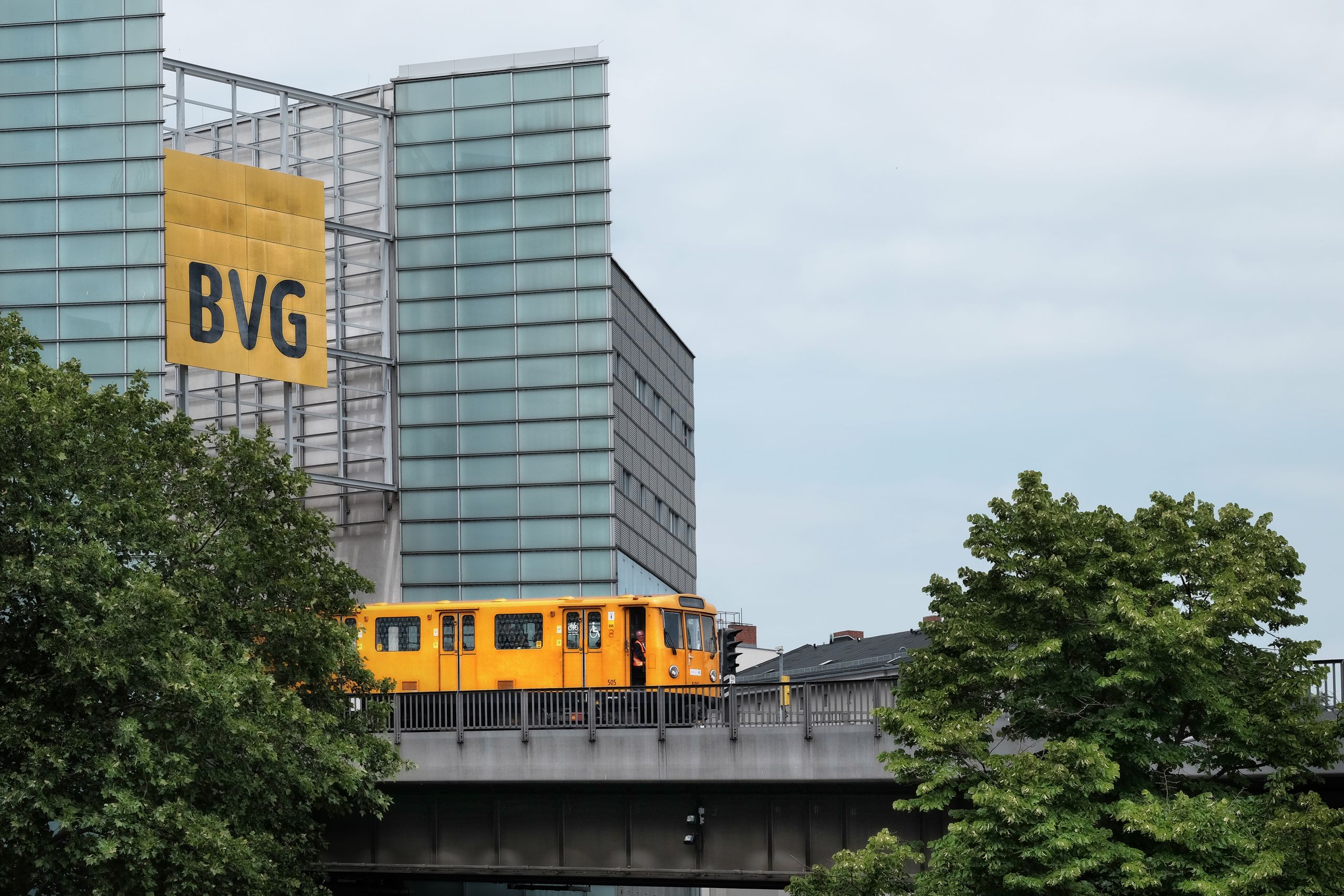 Gelbe U-Bahn der BVG fährt auf einer Hochbahnstrecke vor modernen Gebäuden in Berlin.